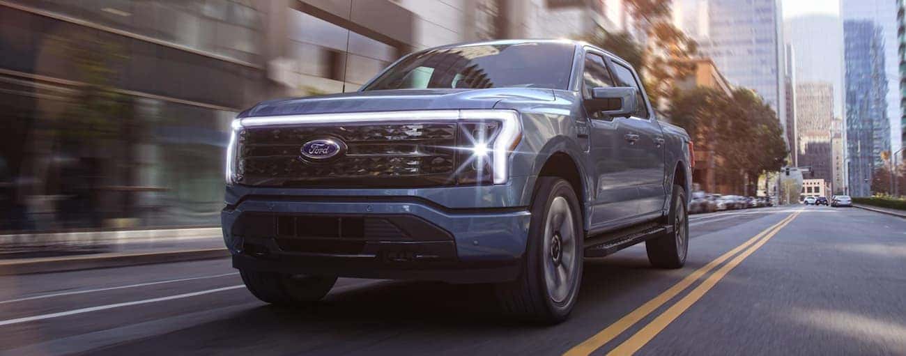 A blue 2022 Ford F-150 Lightning is shown driving down a city street.