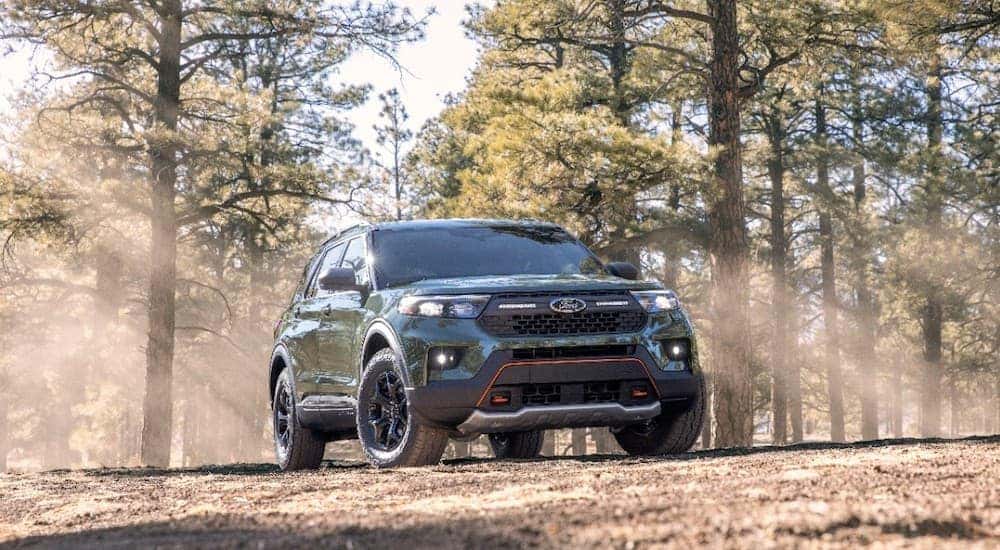 A green 2021 Ford Explorer Timberline is shown parked in the woods with sunlight shining through the trees.