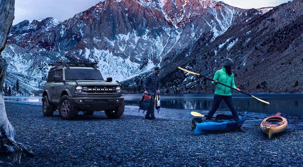 A grey 2021 Ford Bronco is shown on a shore in the mountains next to people going kayaking.