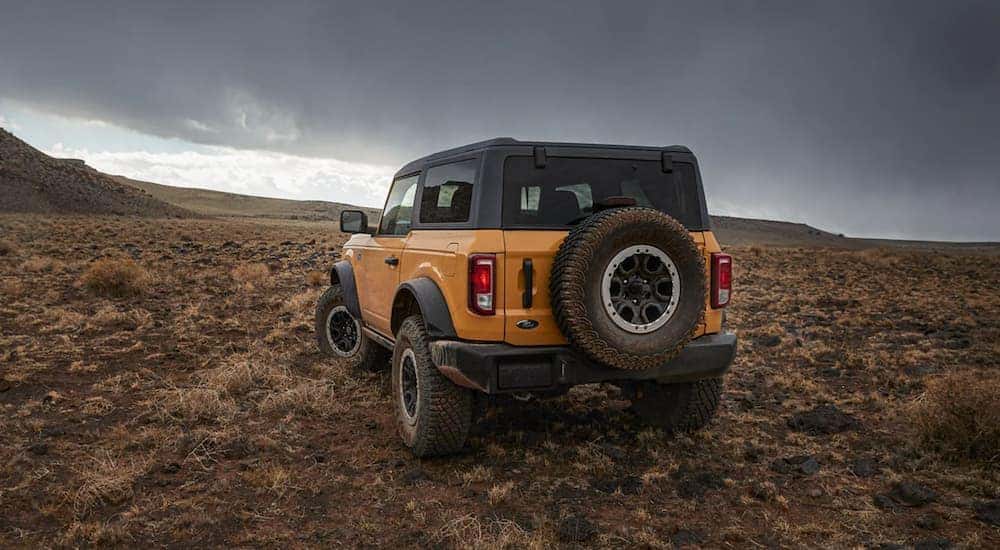 A yellow 2021 Ford Bronco is shown from the back off-roading at sunset.