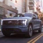 A blue 2022 Ford F-150 Lightning is shown driving down a city street after leaving an electric car dealer in Albany.
