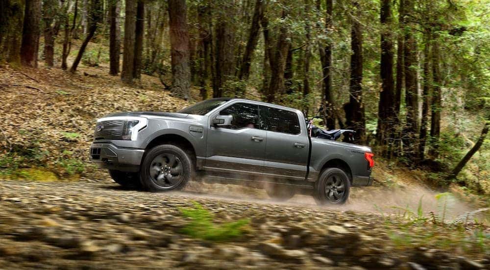 A grey 2022 Ford F-150 Lightning is shown from the side driving through the woods.