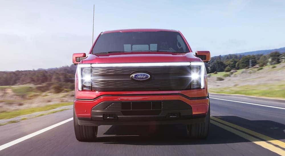 A red 2022 Ford F-150 Lightning is shown from the front driving down a two lane road.
