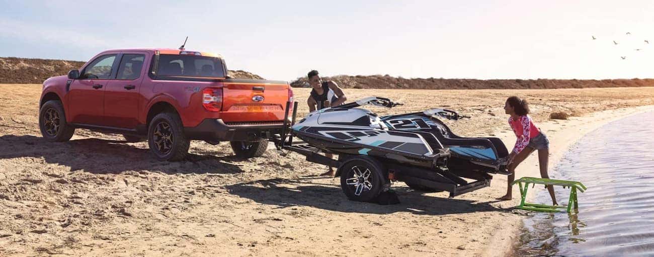 An orange 2022 Ford Maverick is towing a jet-ski on a beach after winning a 2022 Ford Maverick VS 2022 Hyundai Santa Cruz comparison.