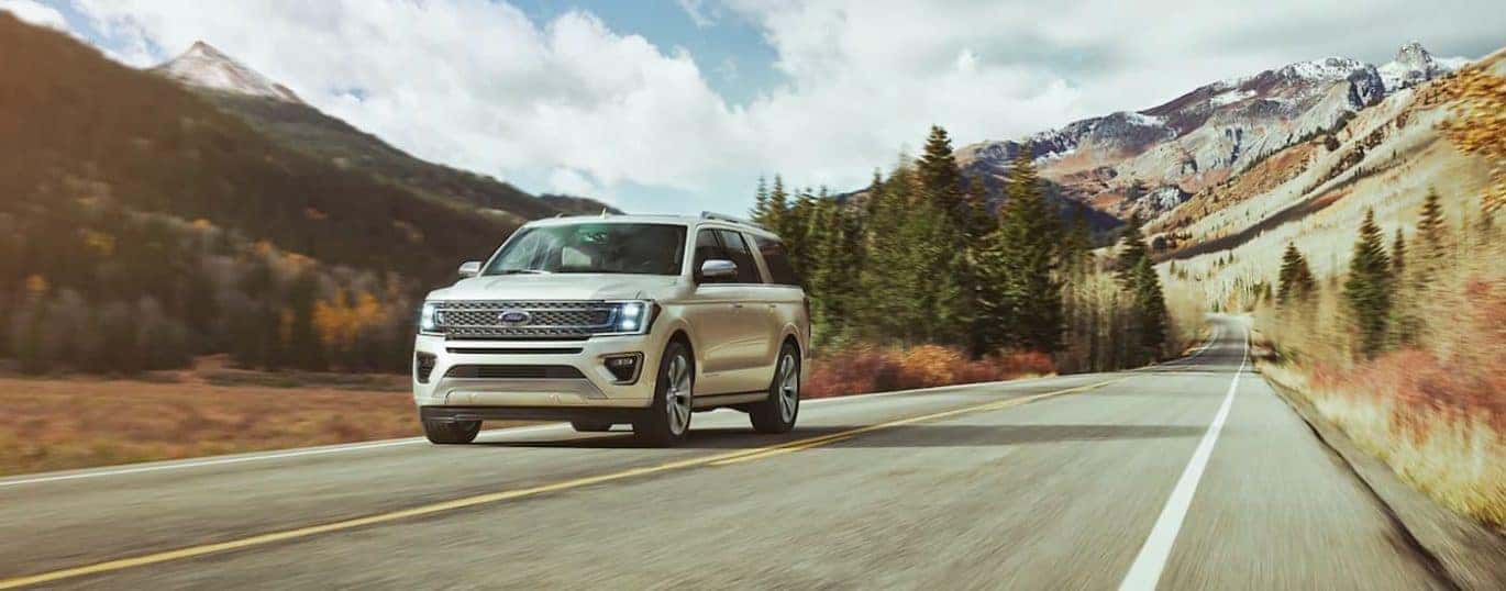 A white 2021 Ford Expedition is shown driving on an empty road with distant mountains.