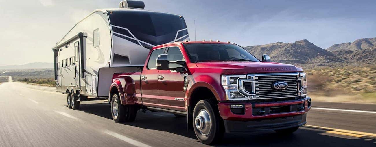 A red 2022 Ford Super Duty is towing a camper on an open highway.
