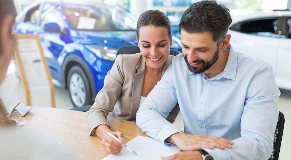 A couple is signing paperwork at a dealership.