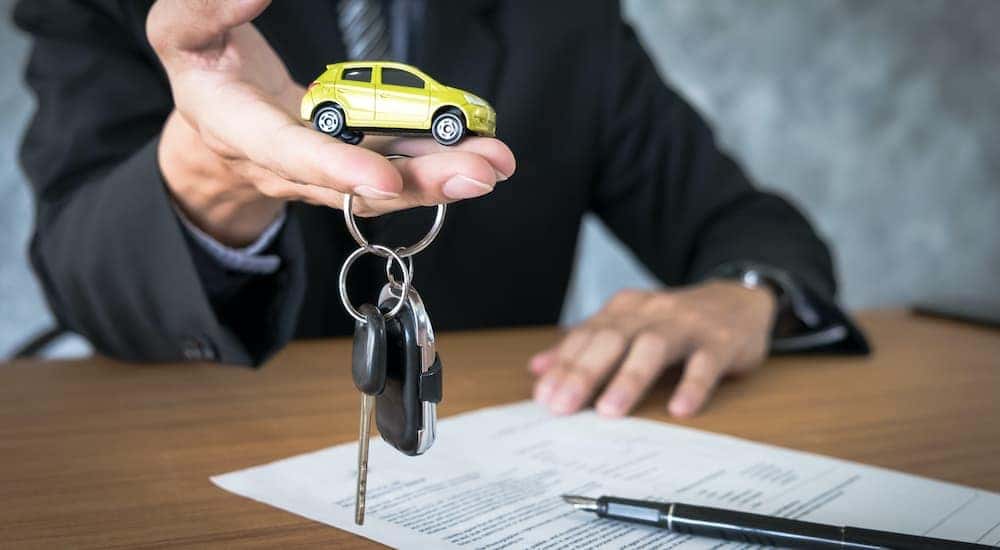 A salesman is holding out a set of keys and a toy car.