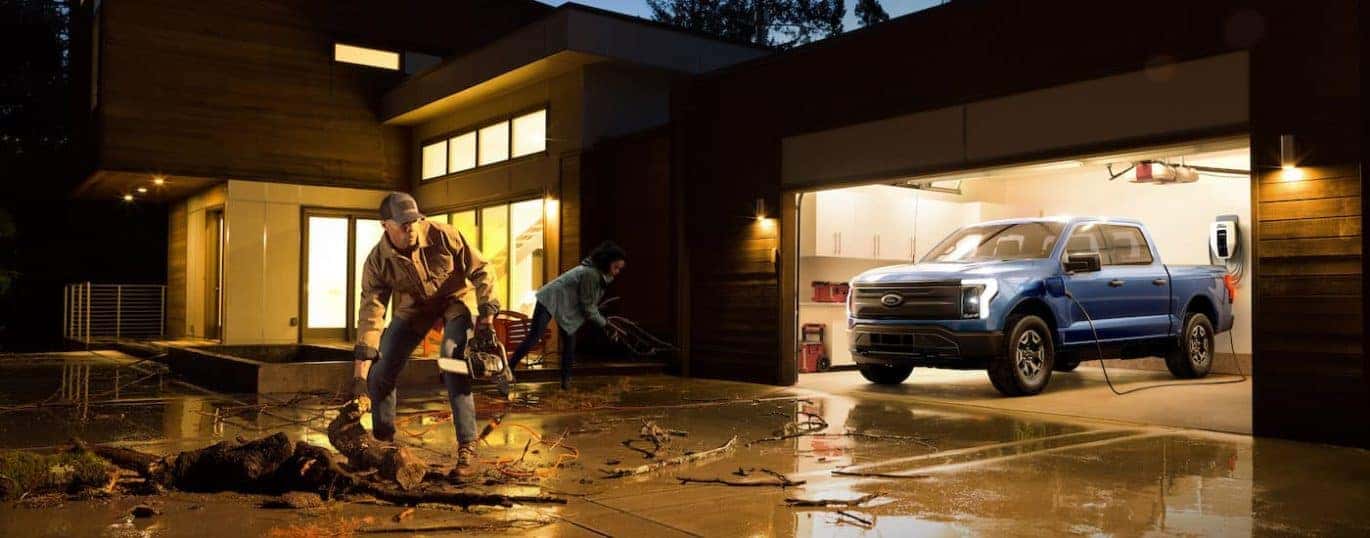 A blue 2022 Ford F-150 Lightning Pro is shown in a garage during a storm.