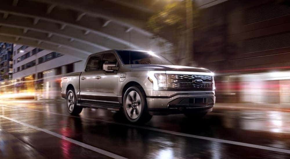 A grey 2022 Ford F-150 Lightning is shown driving through a city after leaving a Ford dealer in Schenectady, NY.
