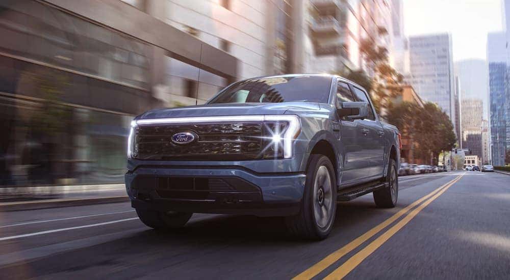A blue 2022 Ford F-150 Lightning is shown from the front driving through a city.