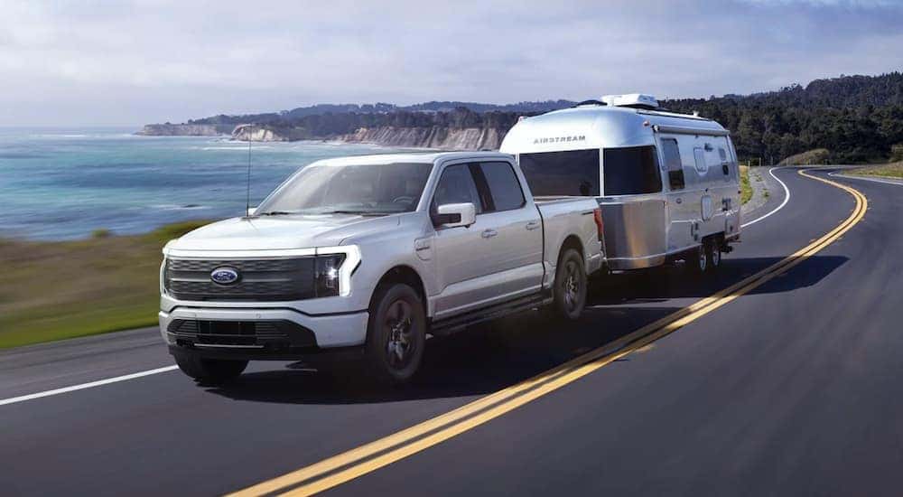 A white 2022 Ford F-150 Lightning is shown towing an Airstream after leaving an electric car dealer in Albany.