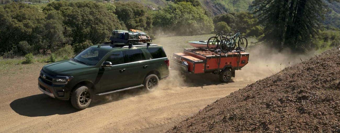 A green 2022 Ford Expedition is towing a trailer on a dirt road in the mountains.