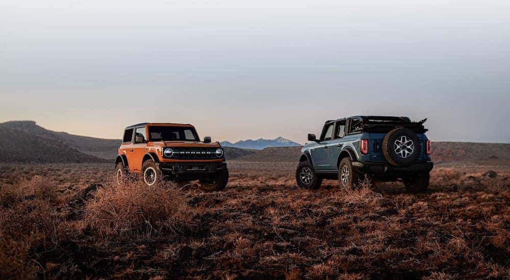 An orange and a blue 2021 Ford Bronco are shown parked in a remote desert area.