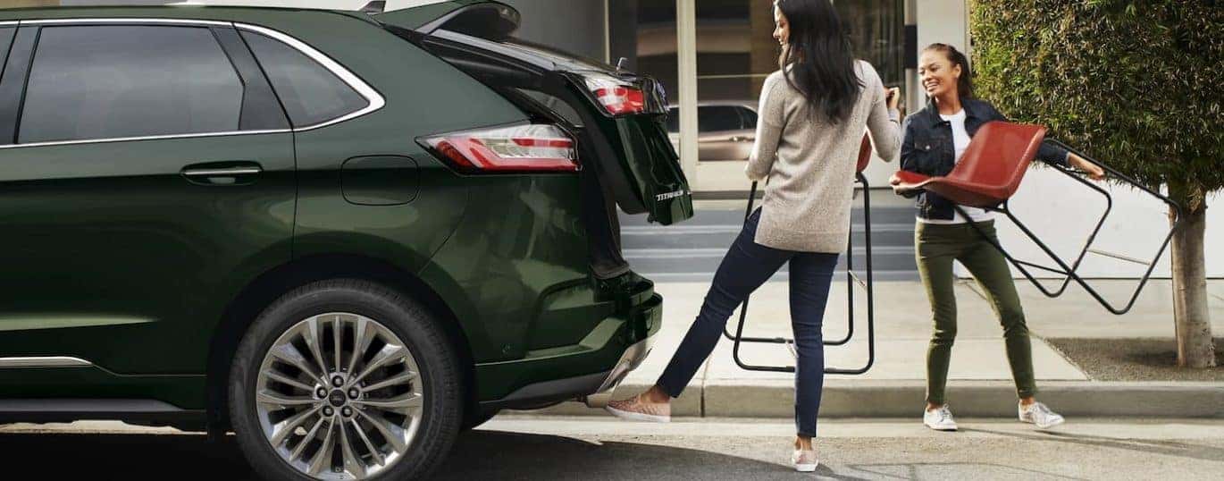 Two people are shown packing chairs into the trunk of a green 2022 Ford Edge Titanium.