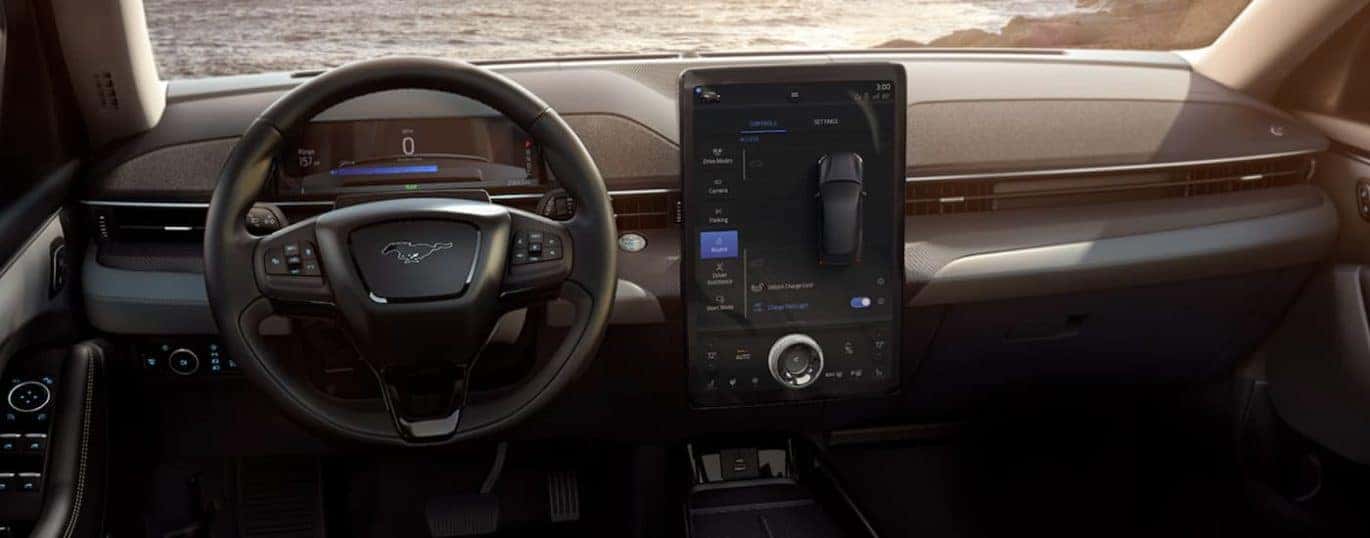 The black interior of a 2022 Ford Mustang Mach-E shows the steering wheel and infotainment screen.