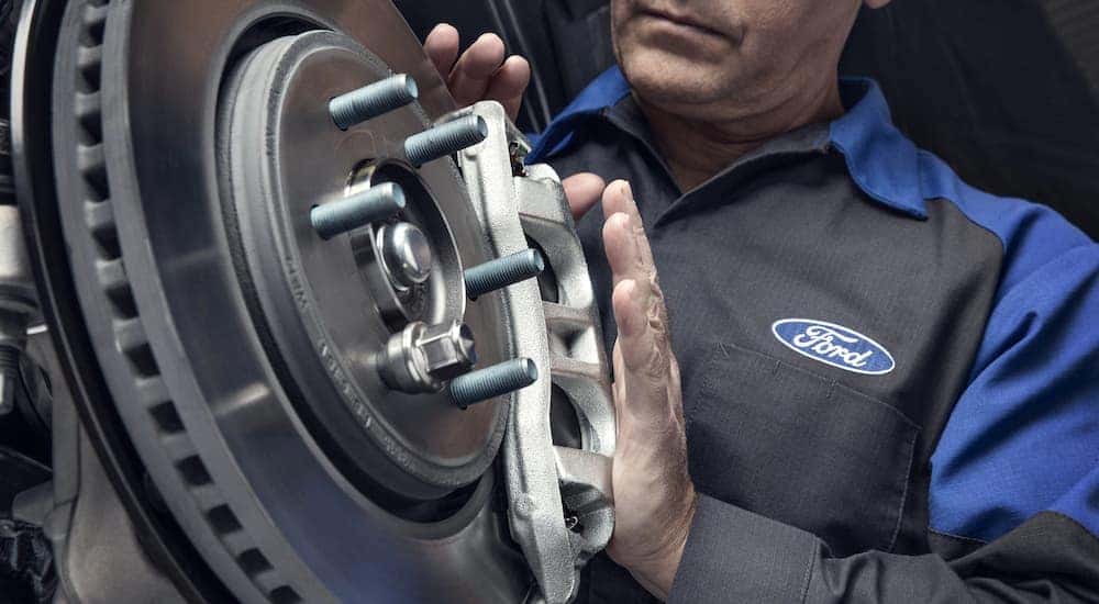 A mechanic at a NY CPO Ford dealer is shown inspecting brakes.