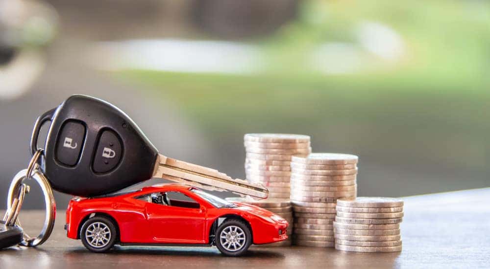 A red toy car is shown next to a set of car keys and coins.