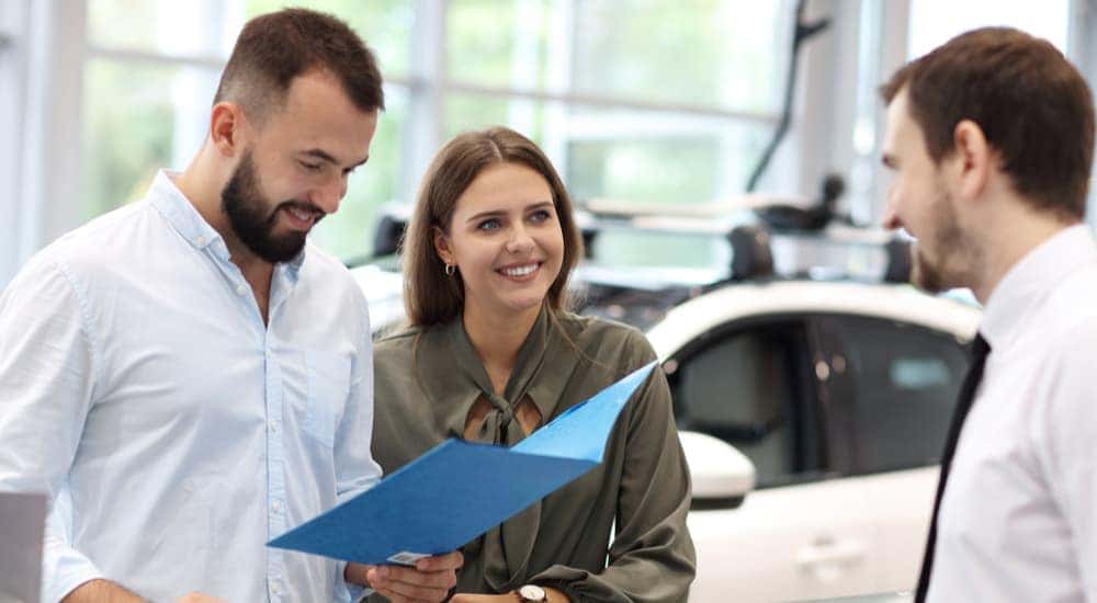 A couple is shown bringing paperwork to a dealership after searching 'how to sell my car.'