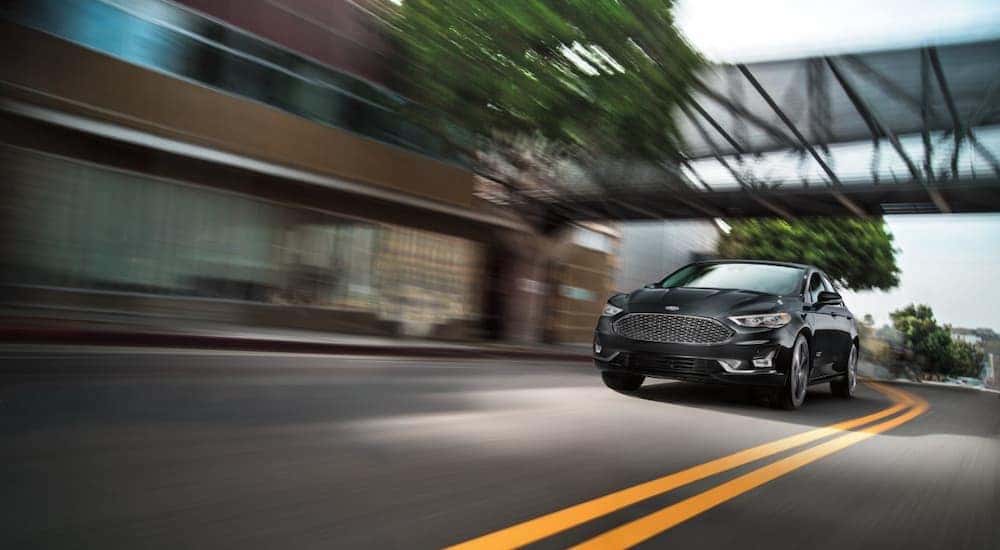A black 2020 Ford Fusion Energi Titanium is shown speeding down a street.