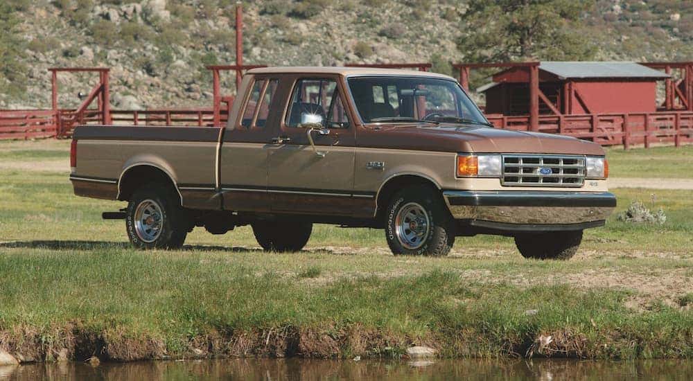 A brown 1987 Ford F-150 is shown parked in a field on a farm.