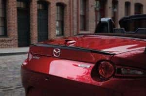 Closeup shot of a stylish red 2019 Mazda MX-5 Miata car with the convertible top down parked across from brick buildings