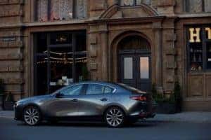 Stylish gray 2019 Mazda3 sedan car parked in front of a city building during the day