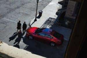 Arial view of a red Mazda6 stopped at an intersection while three pedestrians walk in front of the sedan