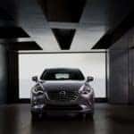 dark gray 2020 Mazda CX-3 parked in a gray parking garage in front of a window with the headlights turned on