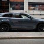 2021 Mazda CX-9 Carbon Edition with black aluminum alloy wheels and Polymetal Gray metallic exterior parked next to a light-colored brick sidewalk