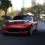 red 2021 Mazda MX-5 Miata Grand Touring trim sports car with a black convertible top parked on black pavement in the shade