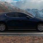 Deep Crystal Blue Mica-colored 2021 Mazda3 hatchback premium trim on black road, snow-capped mountains in background