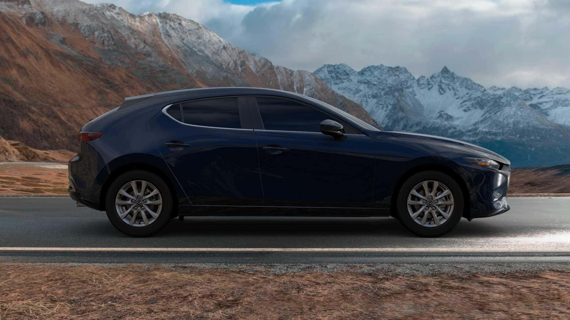Deep Crystal Blue Mica-colored 2021 Mazda3 hatchback premium trim on black road, snow-capped mountains in background