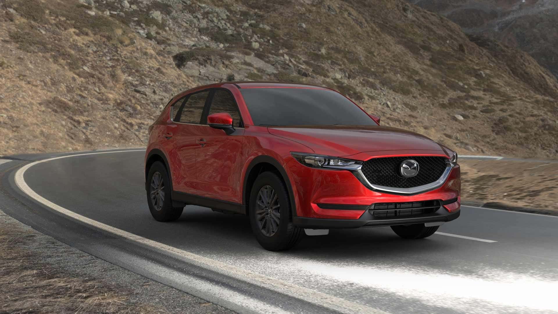 Soul Red Crystal Metallic-colored 2021 Mazda CX-5 sport trim level driving on a black asphalt road, with brown mountains in background