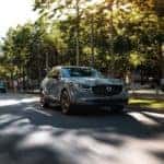 2022 Mazda CX-30 in Machine Gray Metallic driving along a gray road flanked by green trees