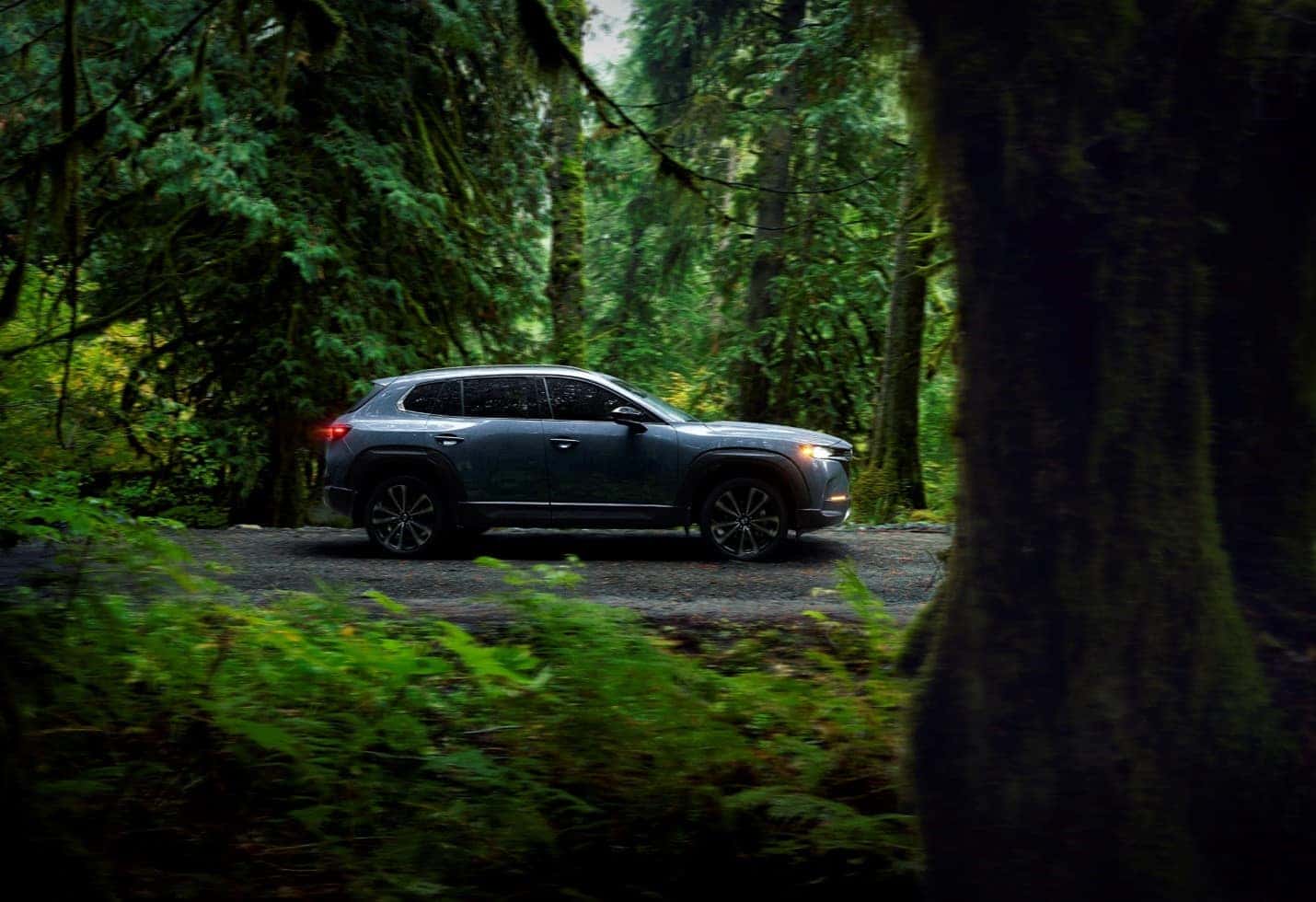 Profile shot of Machine Gray Metallic 2023 CX-50 2.5 Turbo Premium Plus trim level driving through green forest