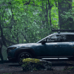 man and woman by a green camping tent in the woods next to a blue 2023 Mazda CX-50 SUV