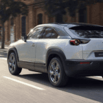 silver Mazda EV vehicle with a black roof driving down a city street