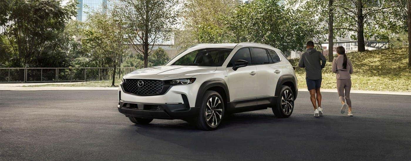 People running near a white 2026 Mazda CX-50 Hybrid