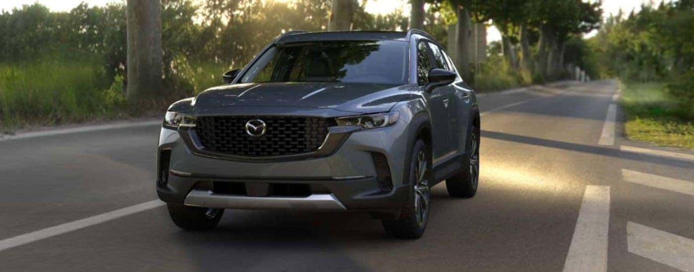A gray 2026 Mazda CX-50 shown driving a tree-lined road.