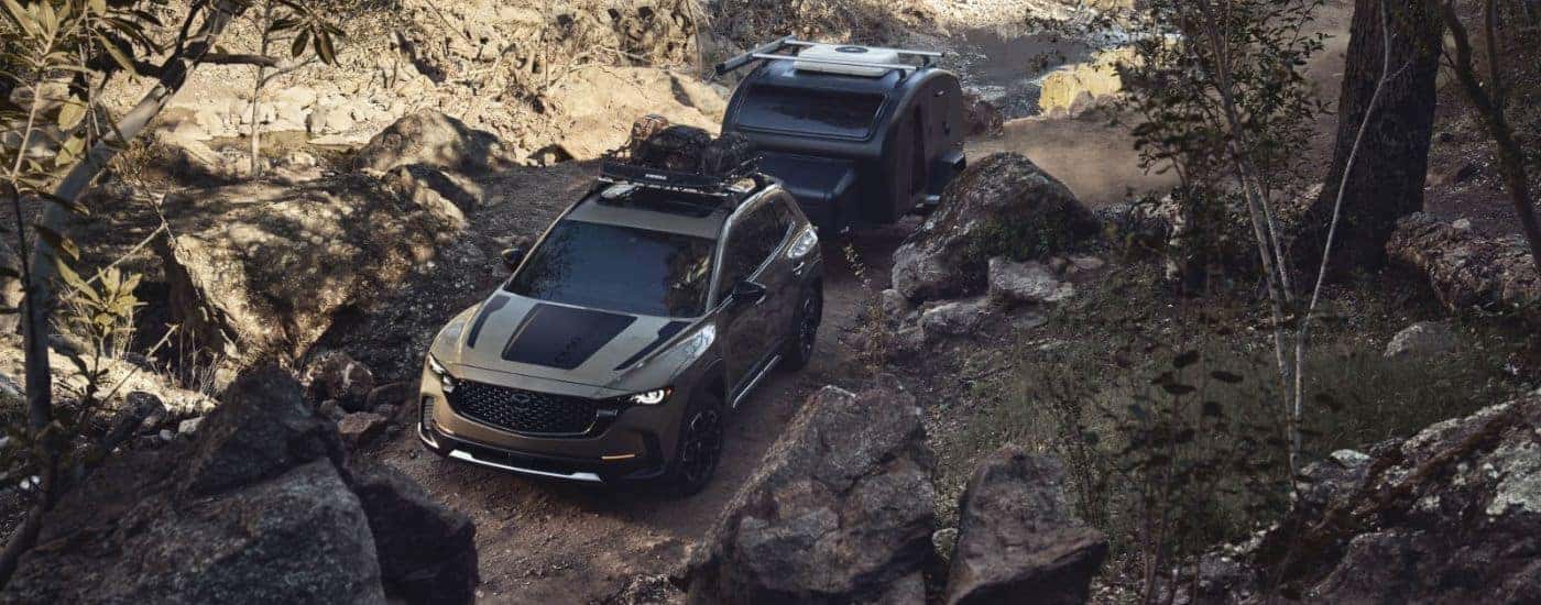 A green 2026 CX-50 2.5 Turbo shown towing a camper on a trail.