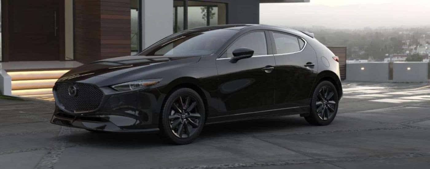A black 2026 Mazda3 Hatchback parked in front of a house.