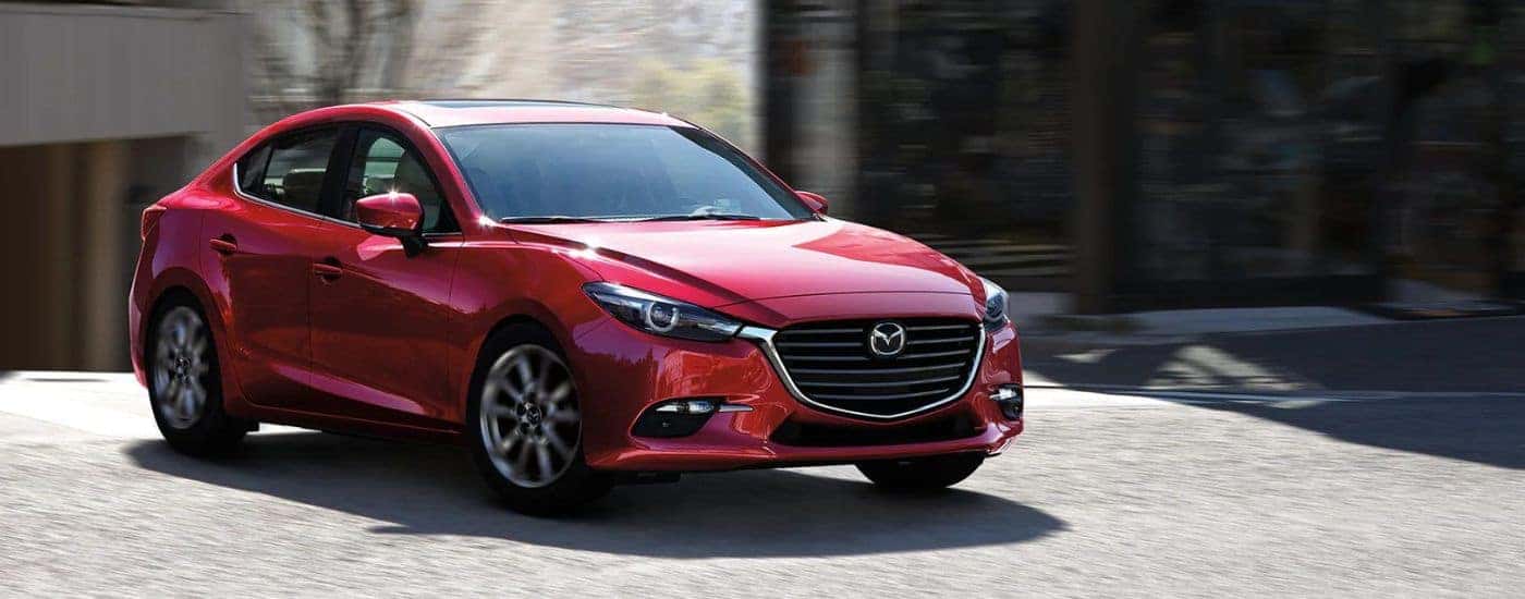 A red 2018 Mazda3 driving by a building.