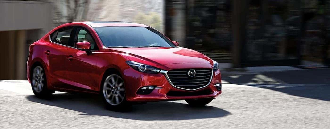 A red 2018 Mazda3 Sedan driving in a city.