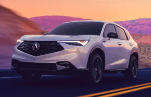A white 2025 Acura ADX SUV driving on a desert highway at sunset, featuring sharp LED headlights, a black diamond-pattern grille with the Acura emblem, and sleek, aerodynamic lines.