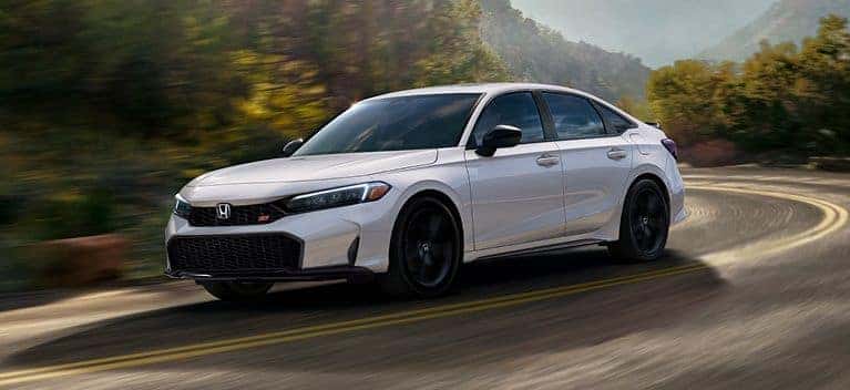 2026 Honda Civic Si sedan in Platinum White Pearl, front three-quarter driving shot on a curving road