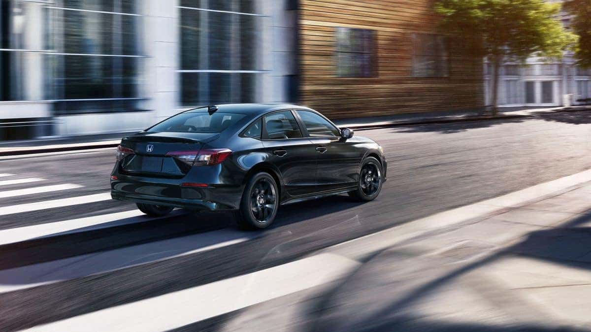 2026 Honda Civic Sport Hybrid sedan in Crystal Black Pearl, rear three-quarter driving shot