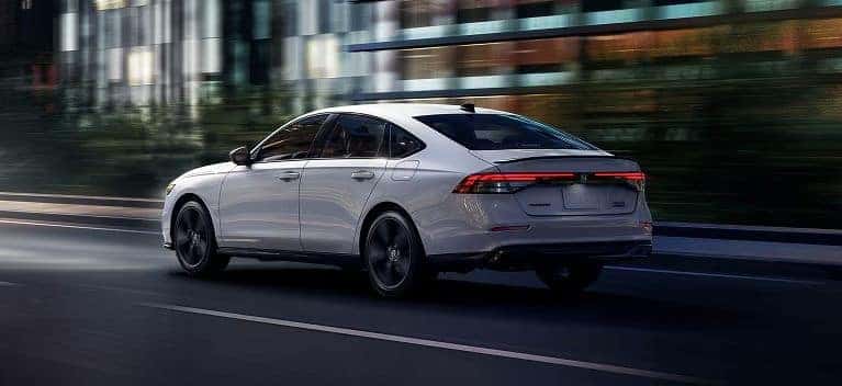 2026 Honda Accord Sport Hybrid sedan in white driving on a city street at dusk