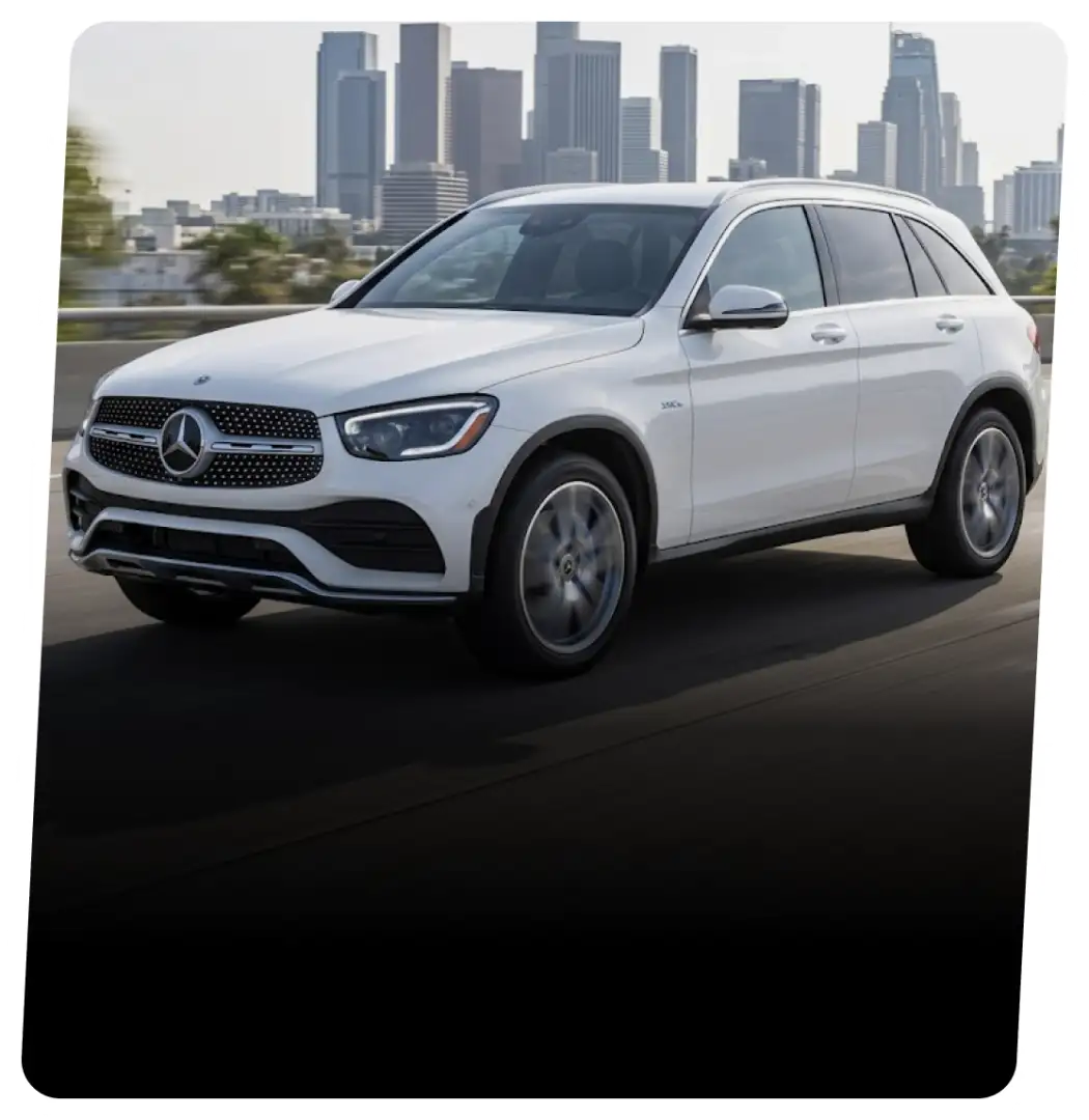 White Mercedes-Benz GLC hybrid SUV on a highway with a city skyline behind it