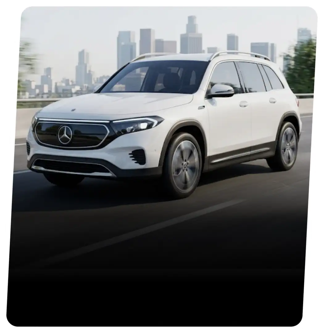 White Mercedes-Benz EQB electric SUV on a highway with a city skyline behind it